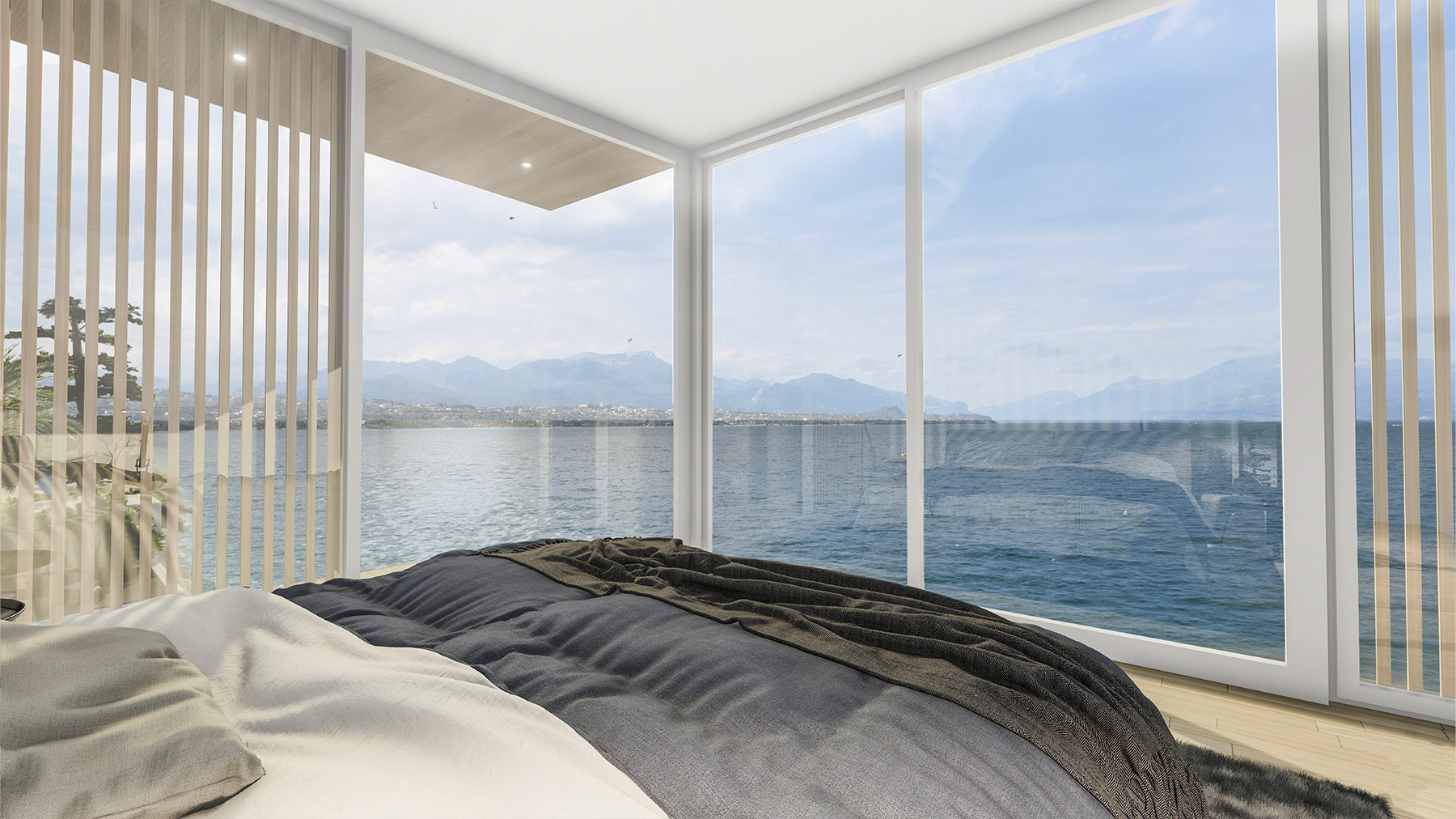 Camera da letto moderna e luminosa con ampie finestre dal pavimento al soffitto che offrono una vista incantevole su un lago e montagne all'orizzonte, arredata con un letto matrimoniale con coperte grigie e beige e pavimento in legno chiaro.